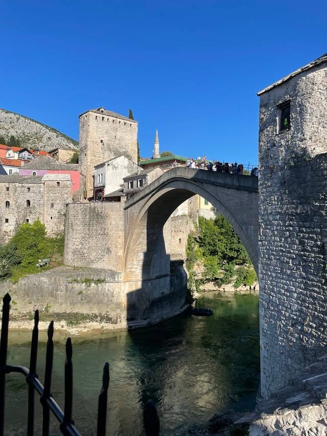 Una imagen del famoso puente de Mostar, rodeado de edificios antiguos y un cielo azul despejado.