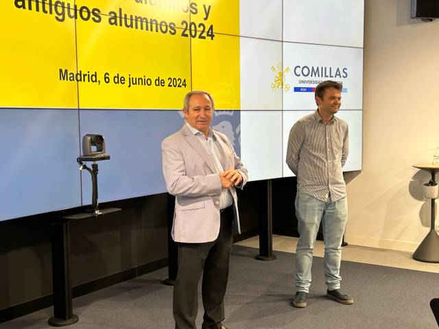 Two men standing in front of a presentation screen at Comillas University with text about a meeting of former students dated June 6, 2024.