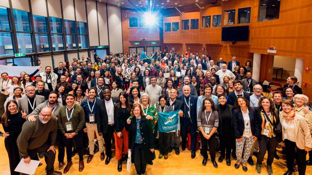 Grupo grande de personas sonriendo en una conferencia con etiquetas de identificación en un auditorio moderno.