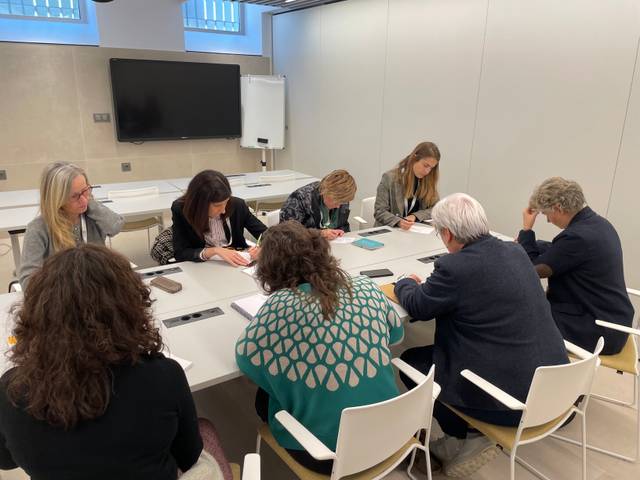 Un grupo de personas se encuentra en una reunión, tomando notas en una mesa de trabajo.