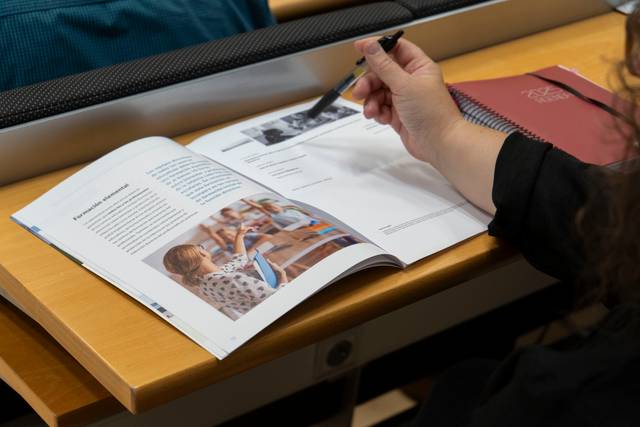 Una persona revisa un libro sobre educación en una mesa de clase.