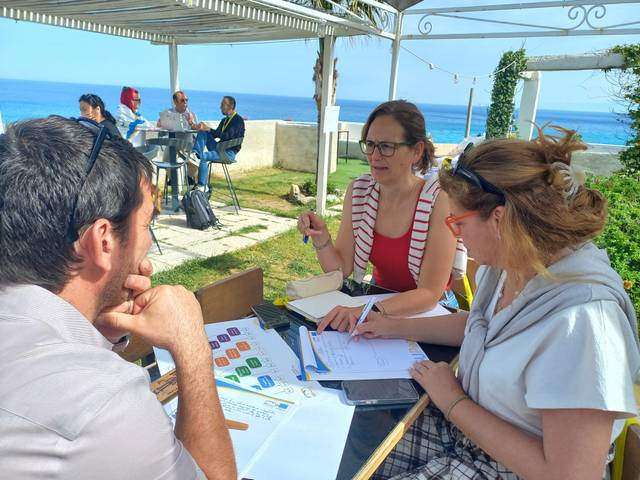 Un grupo de personas se reúne al aire libre para discutir y trabajar en un proyecto frente al mar.