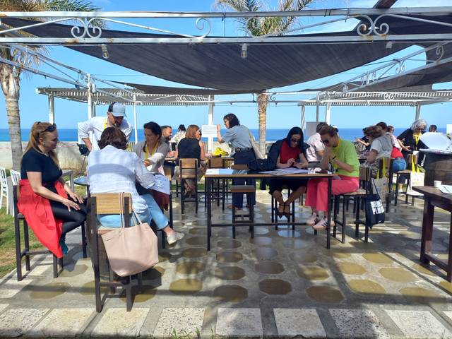 Un grupo de personas interactuando y trabajando en un espacio al aire libre con vistas al mar.