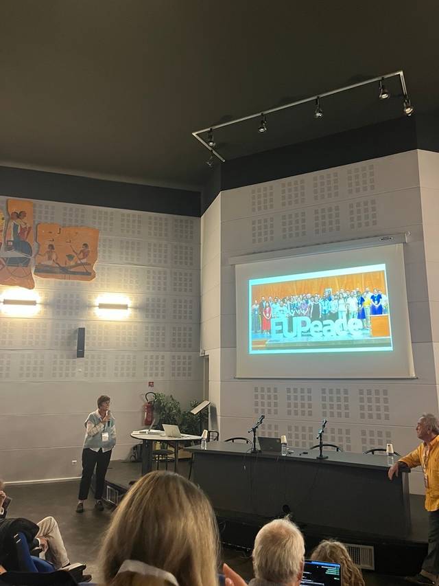 Una presentación en un auditorio con personas en el escenario y un ponente en el frente.