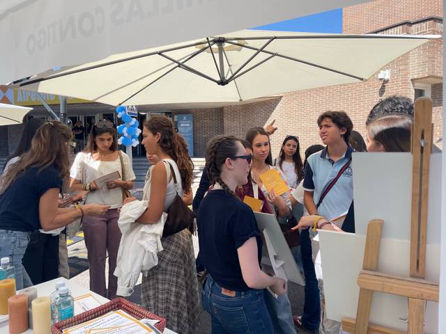 Un grupo de personas interactúa en un evento al aire libre bajo sombrillas.