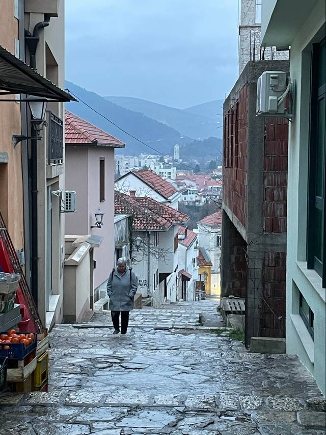 Una persona camina por una empedrada calle en una ciudad montañosa bajo un cielo nublado.