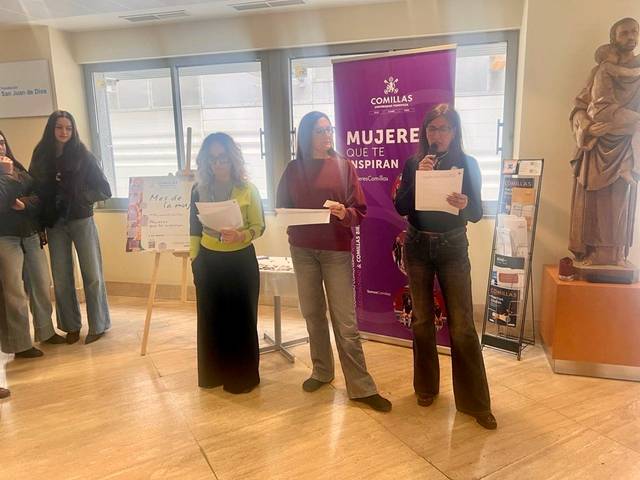Tres mujeres participan en un evento, sosteniendo documentos en un recinto con un cartel sobre mujeres inspiradoras al fondo.