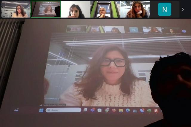 Una reunión en línea proyectada en una pantalla, mostrando varias personas en una videoconferencia.