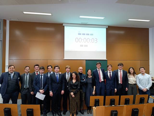 Un grupo de personas vestidas formalmente posando frente a un reloj de cuenta regresiva en un aula.