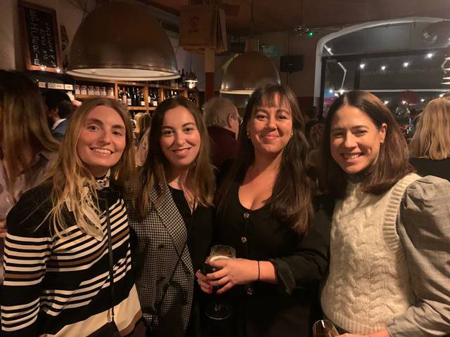 Four women smiling in a bar holding drinks.