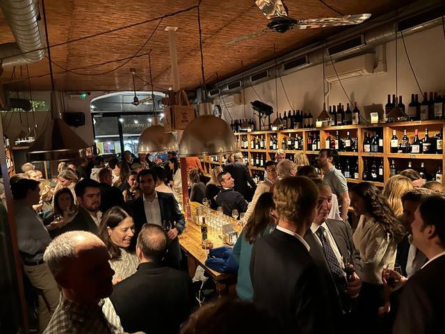 A crowded wine bar event with people engaged in conversations.