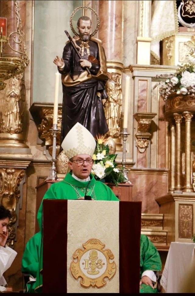 Un sacerdote en un altar rodeado de decoraciones religiosas y una estatua.