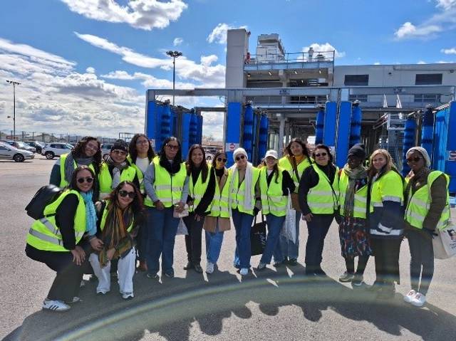 Un grupo de personas con chalecos amarillos se encuentra en una zona industrial bajo un cielo parcialmente nublado.