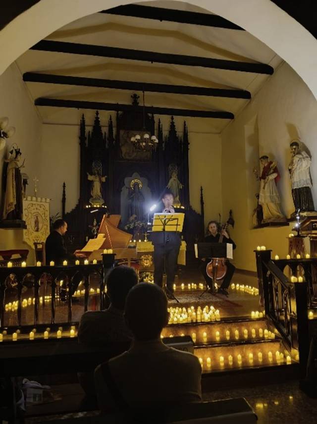 Un grupo de músicos actúa en una iglesia iluminada suavemente por velas en un ambiente íntimo.