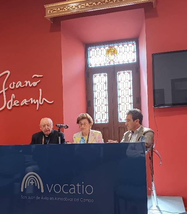 Una tertulia en un evento con tres personas sentadas frente a un panel en un ambiente académico.