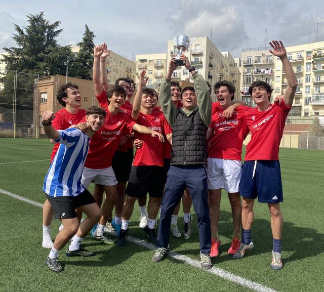 Un grupo de jóvenes celebra con alegría la victoria en un campo de fútbol sosteniendo un trofeo.