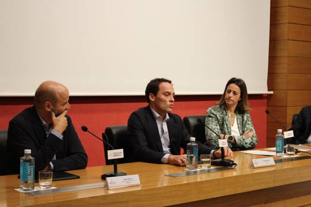 Three professionals sitting at a panel discussion table in a conference room, engaged in a conversation.