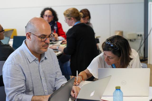 A man and a woman working on laptops in a busy office environment