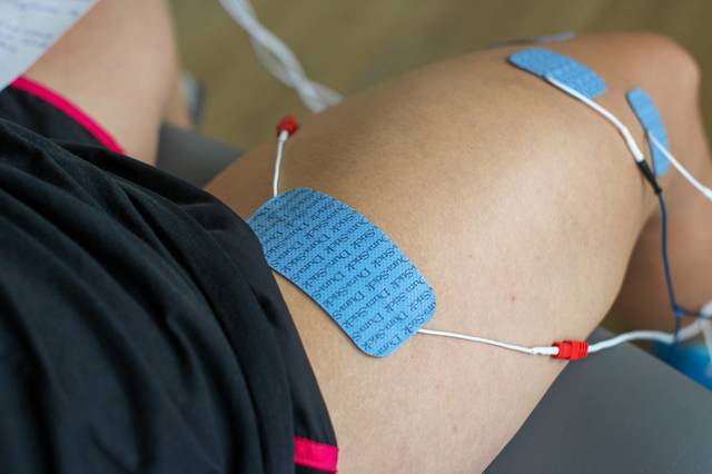 Close-up of a knee undergoing electrotherapy with two blue electrode pads attached.