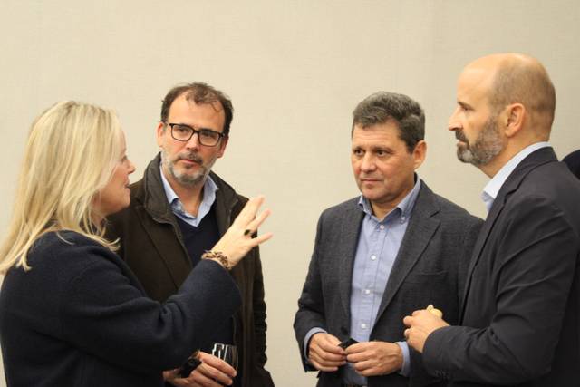 A woman gestures while talking to three men at a social gathering.