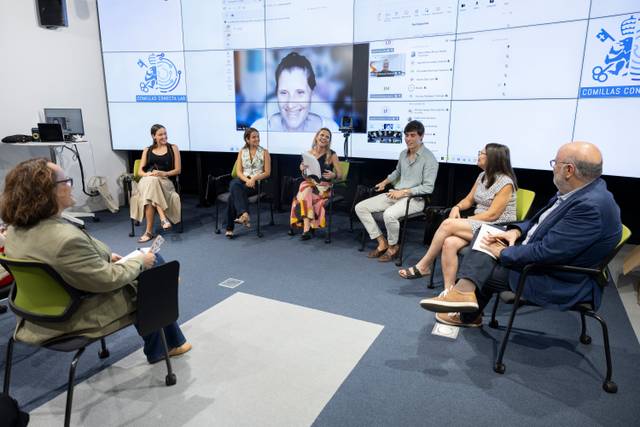Un grupo de personas participa en una mesa redonda frente a una pantalla gigante en un entorno académico.
