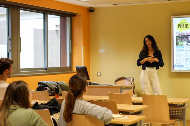 A woman is giving a presentation in a classroom with several students listening.