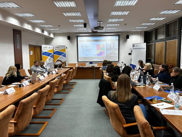 Una reunión de trabajo en un aula con varias personas sentadas alrededor de una mesa grande.