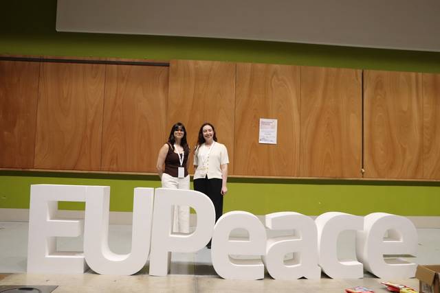 Dos mujeres posan junto a letras grandes que forman la palabra 'EUPeace'.