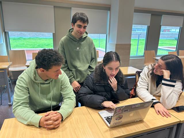 Cuatro jóvenes estudian juntos frente a un ordenador en un aula.