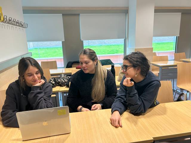 Tres estudiantes observan atentas una laptop en un ambiente de aula.