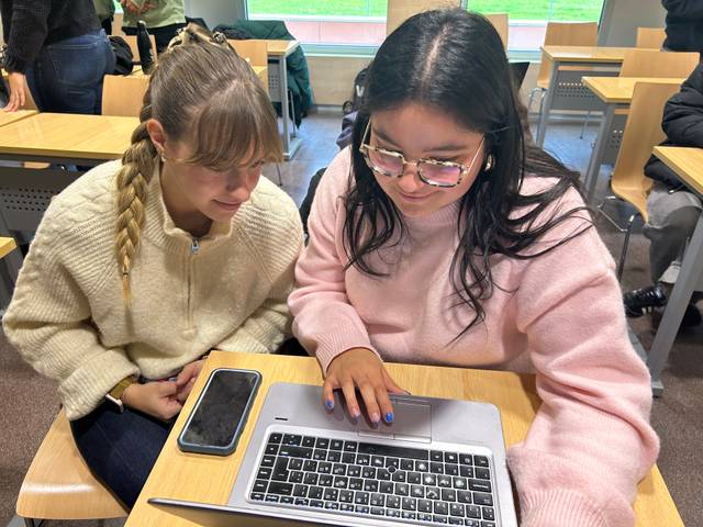 Dos jóvenes observan una computadora portátil en un entorno académico.