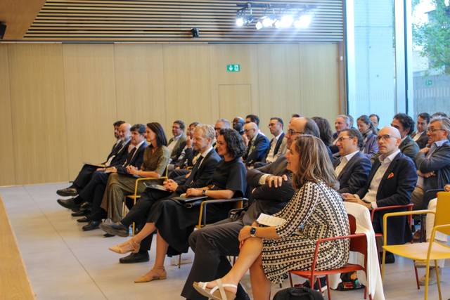 Un grupo de personas sentadas en un evento, prestando atención a un orador en un ambiente moderno.