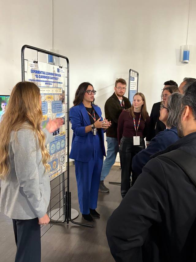 Un grupo de personas escucha a una mujer que está presentando un proyecto en un evento.