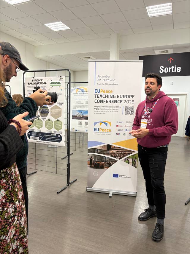 Un hombre habla frente a un cartel sobre una conferencia en un evento público.