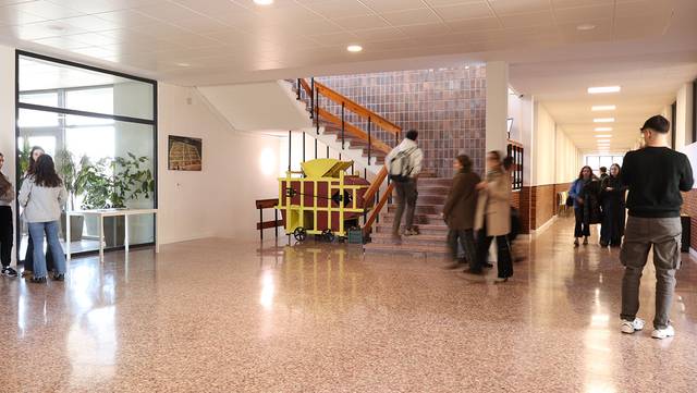 Una imagen de un pasillo escolar con estudiantes y escaleras al fondo.