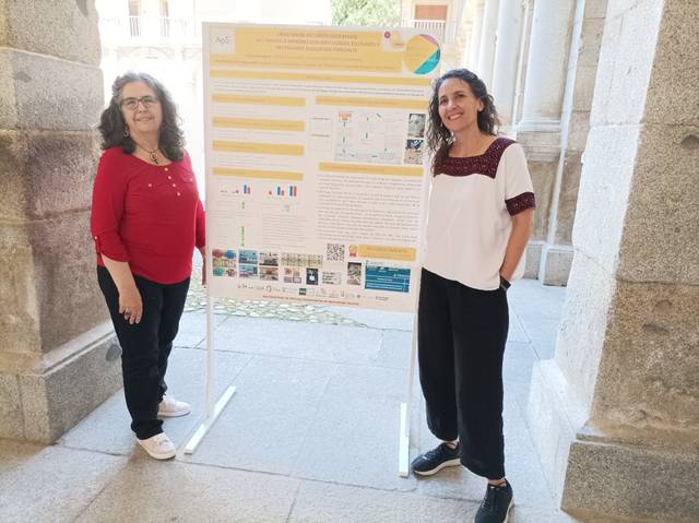 Two women standing beside a presentation poster in a hallway with arches.