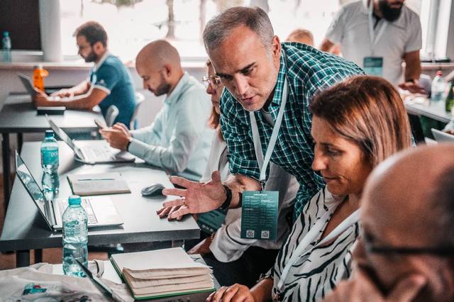 A mature man is discussing with a woman at a busy conference table while other participants are focused on their tasks.