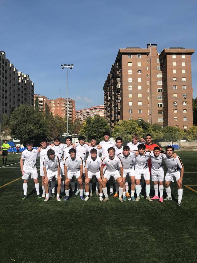 Un equipo de fútbol masculino posa en el campo antes de un partido, con edificios altos al fondo.