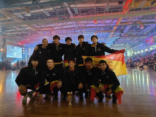 Un grupo de jóvenes posa con una bandera de España y un trofeo en un evento deportivo o de competencia.