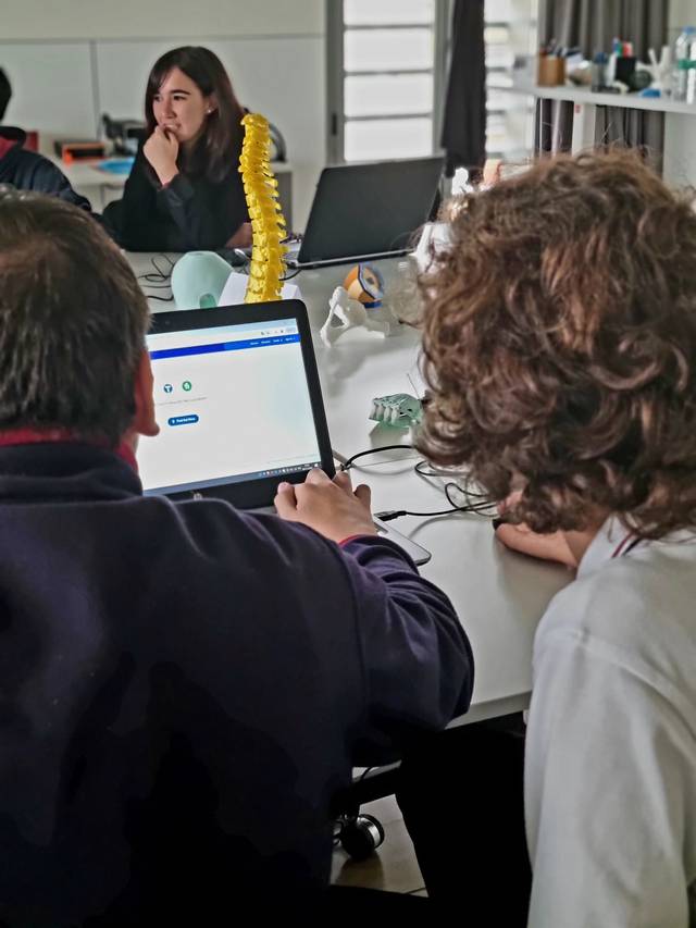 Personas trabajando en una oficina con un hombre y una mujer sentados frente a una computadora, mostrando una pantalla con gráficos, mientras otra mujer observa al fondo.