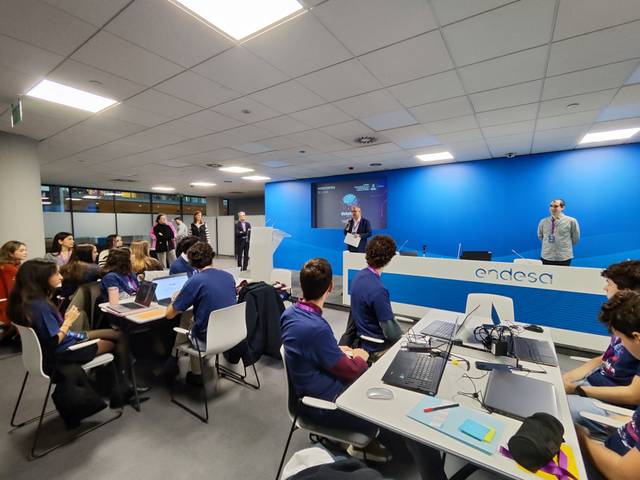 Un grupo de jóvenes estudiantes sentados en un aula moderna escuchando a un orador durante un evento.