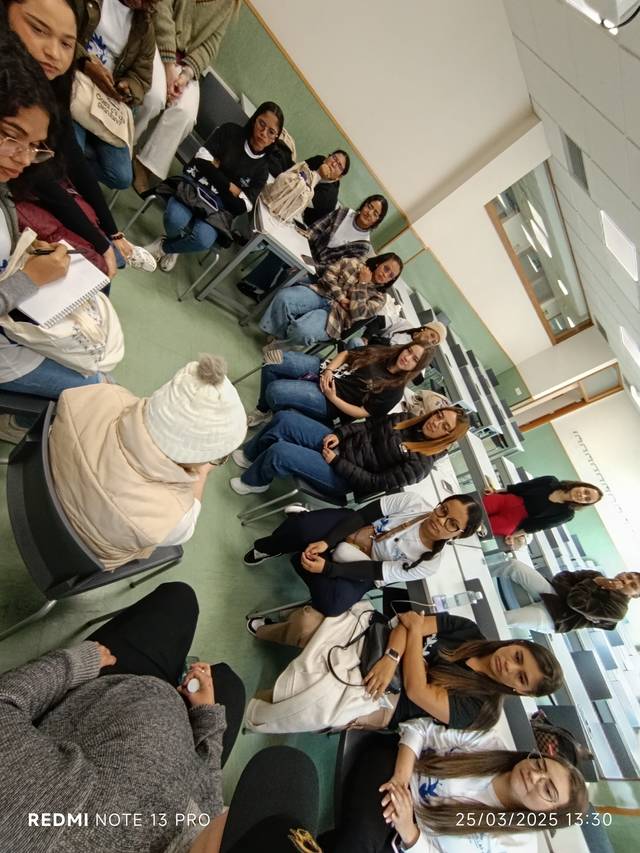 Un grupo de personas sentadas en un aula, conversando y tomando notas.