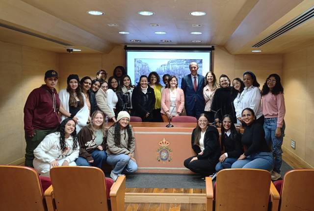 Grupo de personas posando en un salón con una presentación al fondo.