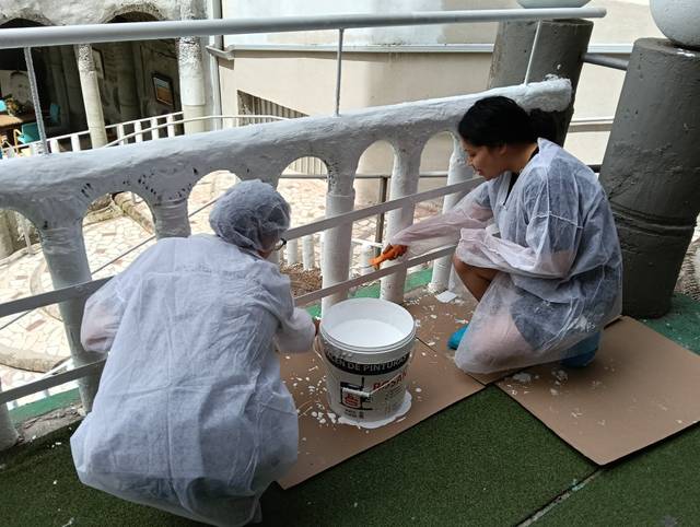 Dos personas están pintando una baranda en un espacio al aire libre.