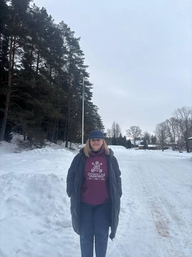 Una persona de pie en una calle nevada rodeada de árboles.