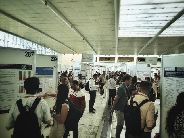 La imagen muestra a un grupo de personas en una exposición con varios paneles informativos y posters en un recinto amplio.