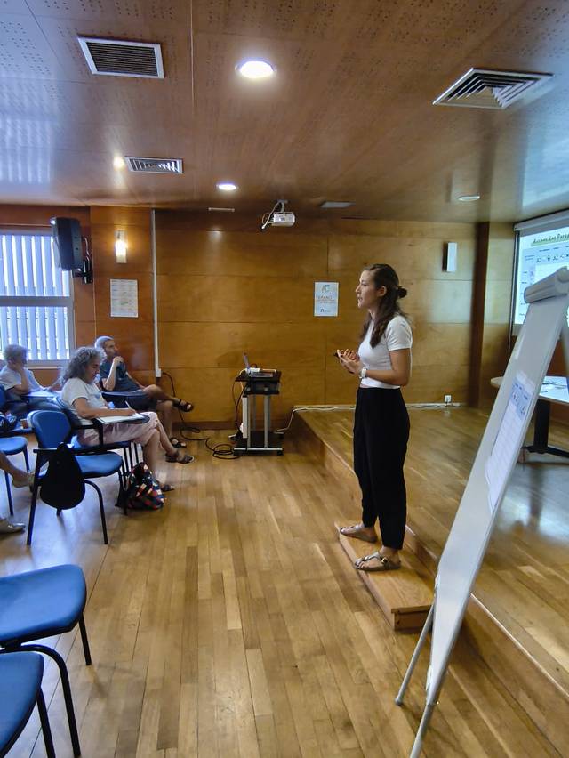 Una mujer está dando una presentación frente a un grupo de personas sentadas en un aula.