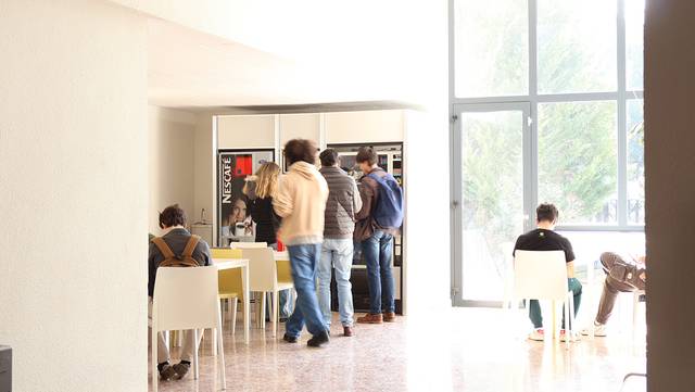 Un grupo de personas en un área de descanso con máquinas expendedoras y mesas.