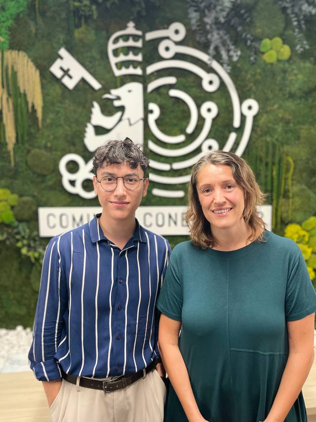 Dos personas posan sonrientes frente a un mural decorativo en un ambiente de oficina.