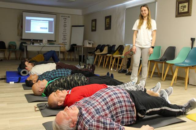 Un grupo de personas realiza ejercicios en el suelo mientras una instructora observa.